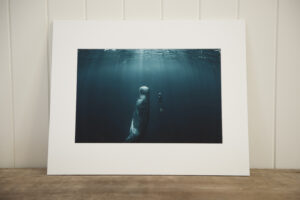 Fine art image of a diver and a whale on smooth matt rag photo paper with a custom white matt leaning against a wall on a wooden shelf