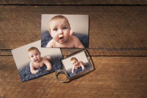 Two magnets with images of baby as well as a keying with same baby laying on wooden table top