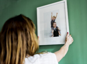 Woman hanging a white photo framed image of a man and a boy on a green wall