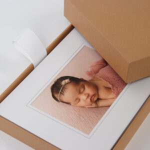 Craft box open on a white table with a pile of matted print inside of it