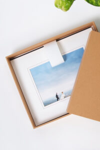 Craft box open on a white table with a pile of matted print inside of it