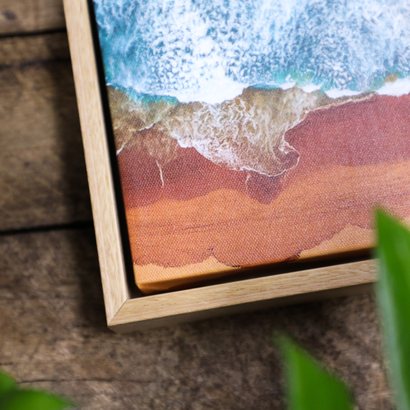 Close up of the corner of a oak float framed canvas print of a beach