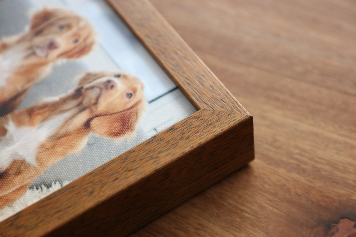 Corner of a walnut framed canvas print of two dogs