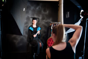 Photographer in studio taking a photo of a graduate holding her diploma