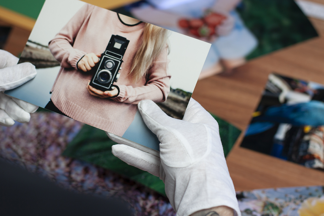 White cotton gloves holding a Kodak lustre print of a woman holding a medium format camera