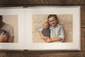 Linen photo album open on wooden box to a page with a printed photo of a boy and his baby brother